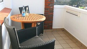 Ein kleiner Balkon mit einem runden Holztisch und zwei Korbstühlen, einer Ziegelwand und Blick auf die Stadt.
