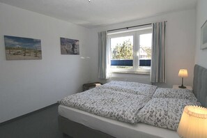 Une chambre à coucher avec un lit, une fenêtre avec des rideaux, une lampe et deux tableaux accrochés au mur.