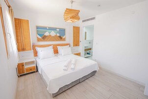 Una habitación de hotel moderna con una cama grande, cabecera de madera y un cuadro de montañas.
