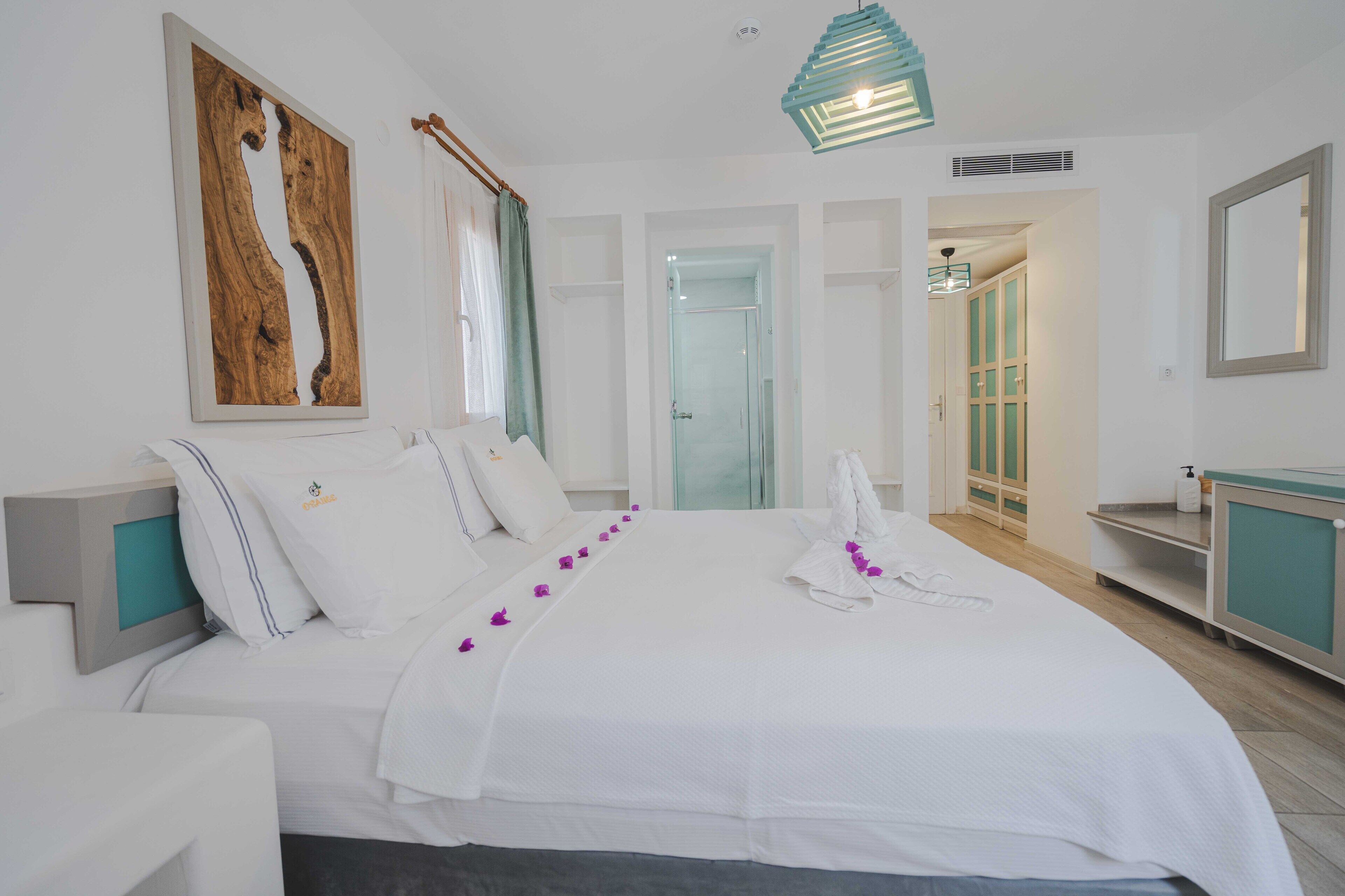 A spacious bedroom with a large bed, a wooden artwork, a bathroom with a glass door, and a teal-toned vanity.