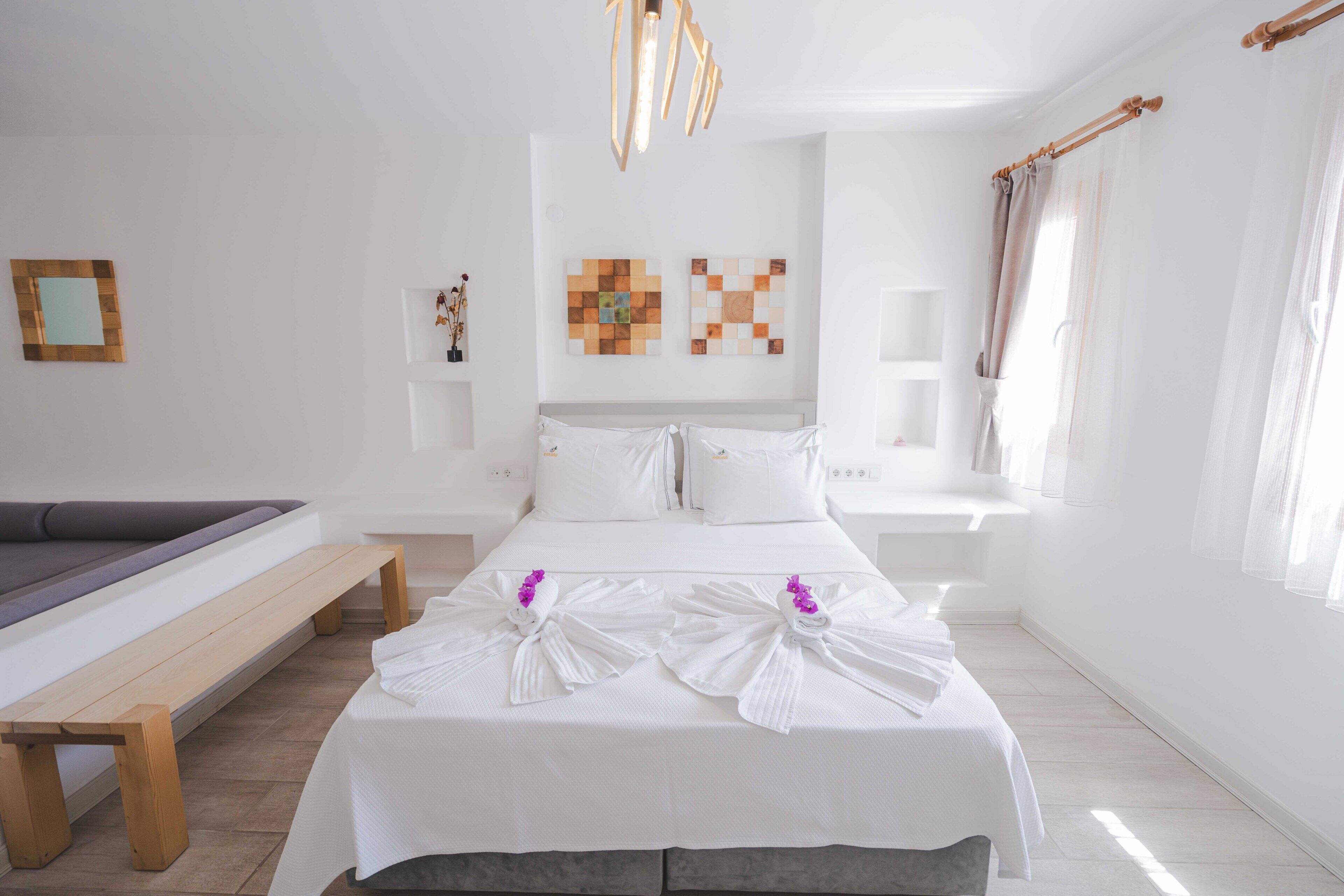 A hotel room with a bed, a bench, a wall-mounted artwork, and a window with curtains.