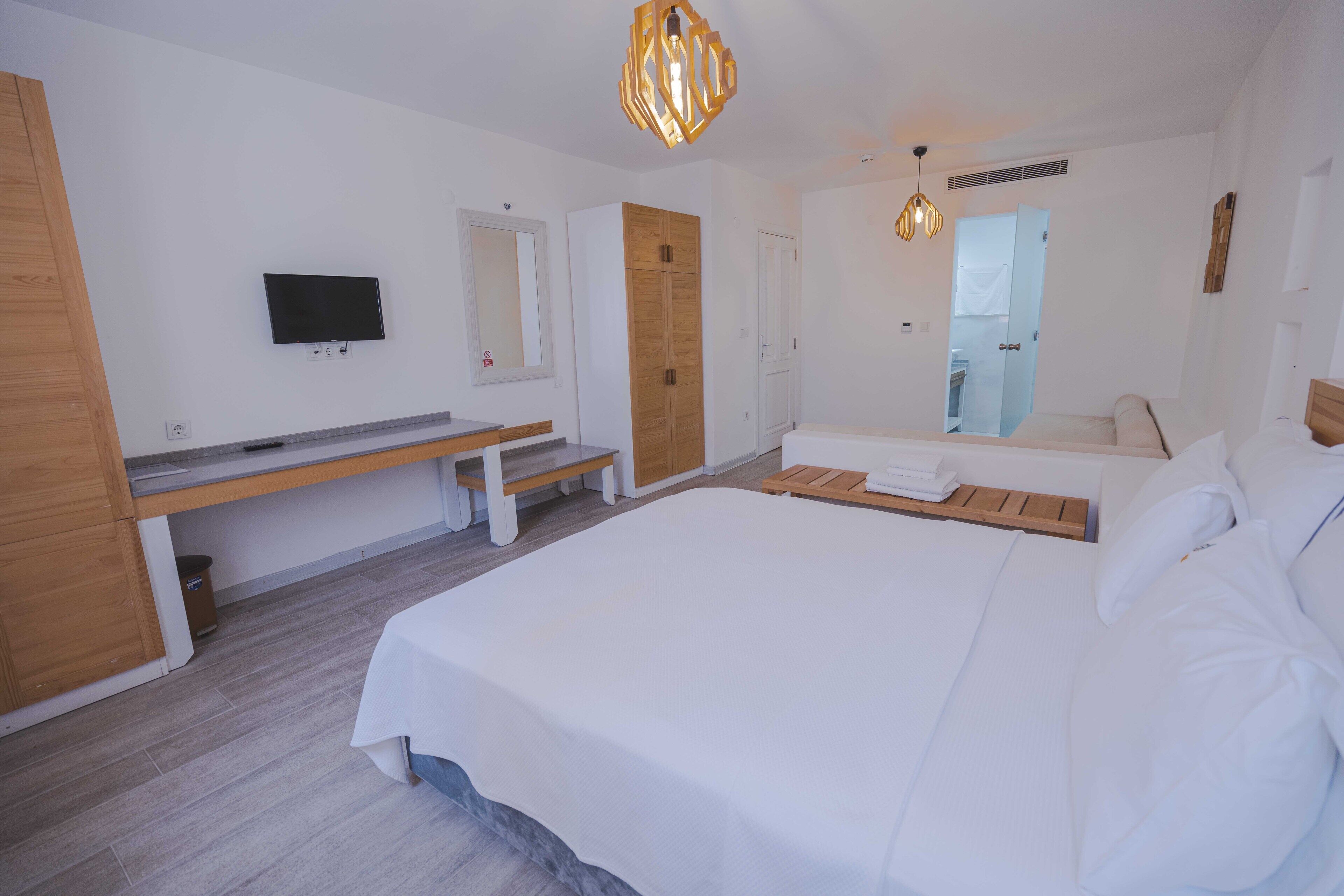 A modern bedroom with a large bed, a bench, a TV, and a wardrobe.