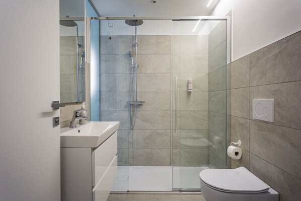 Une salle de bain moderne avec une douche à parois de verre, un lavabo blanc et des toilettes.
