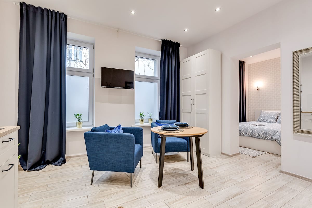 Una sala de estar moderna con dos sillones azules, una mesa redonda de madera y un televisor instalado en la pared.