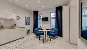 A modern kitchen with white cabinets, a clock, and a flat-screen TV. There is a dining area with two blue chairs and a small round table.