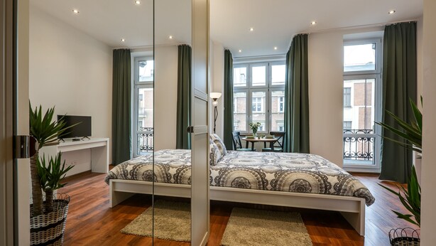 A modern bedroom with a large bed, a desk, and a balcony with a view.