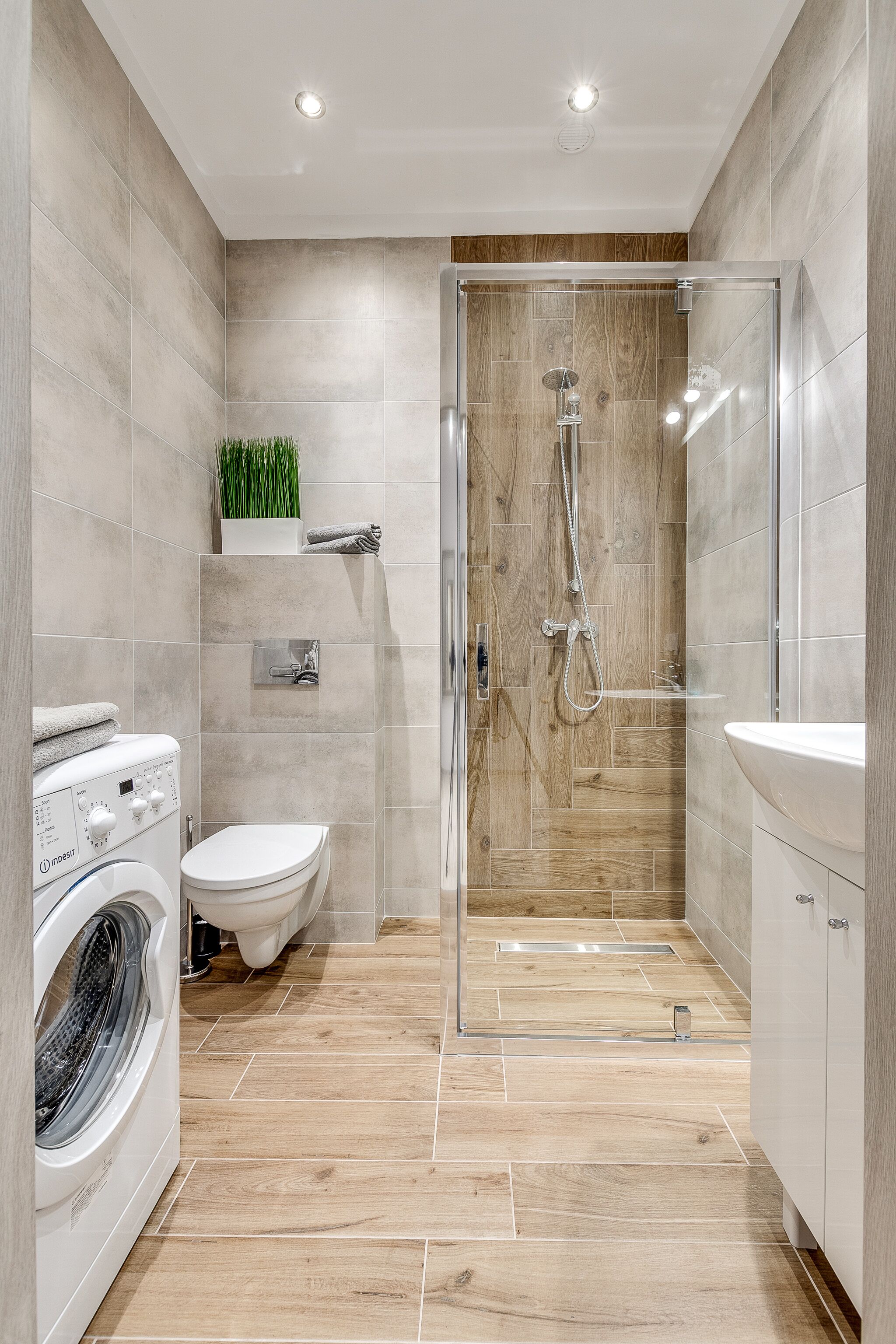 Un baño moderno con ducha acristalada, lavadora e inodoro.