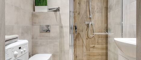 Un baño moderno con ducha acristalada, lavadora e inodoro.