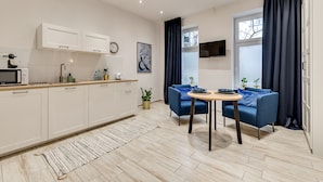 A modern kitchen with white cabinets, a microwave, and a sink. There is a dining area with a blue sofa and a small table.