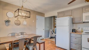 Eine moderne Küche mit einem weißen Kühlschrank, Holzschränken und einem Essbereich mit einem Holztisch und Metallstühlen.