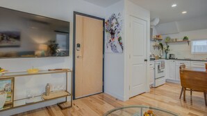 A modern kitchen with white cabinets, a wooden dining table, and a glass coffee table. - 1BR Downtown Urbanitydining, Drink, Cafes & Escape (Colorado Springs)