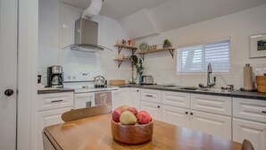 A kitchen with white cabinets, a wooden dining table, and a fruit bowl. - 1BR Downtown Urbanitydining, Drink, Cafes & Escape (Colorado Springs)