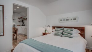 A bedroom with a bed, a nightstand, a lamp, and a view into the kitchen. - 1BR Downtown Urbanitydining, Drink, Cafes & Escape (Colorado Springs)