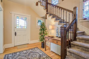 A staircase with a wooden handrail and carpeted steps, a white door with a stained glass window, and a Christmas tree with ornaments. - 5bddowntown Victorian Charmhot Tub, Firepit (Colorado Springs)