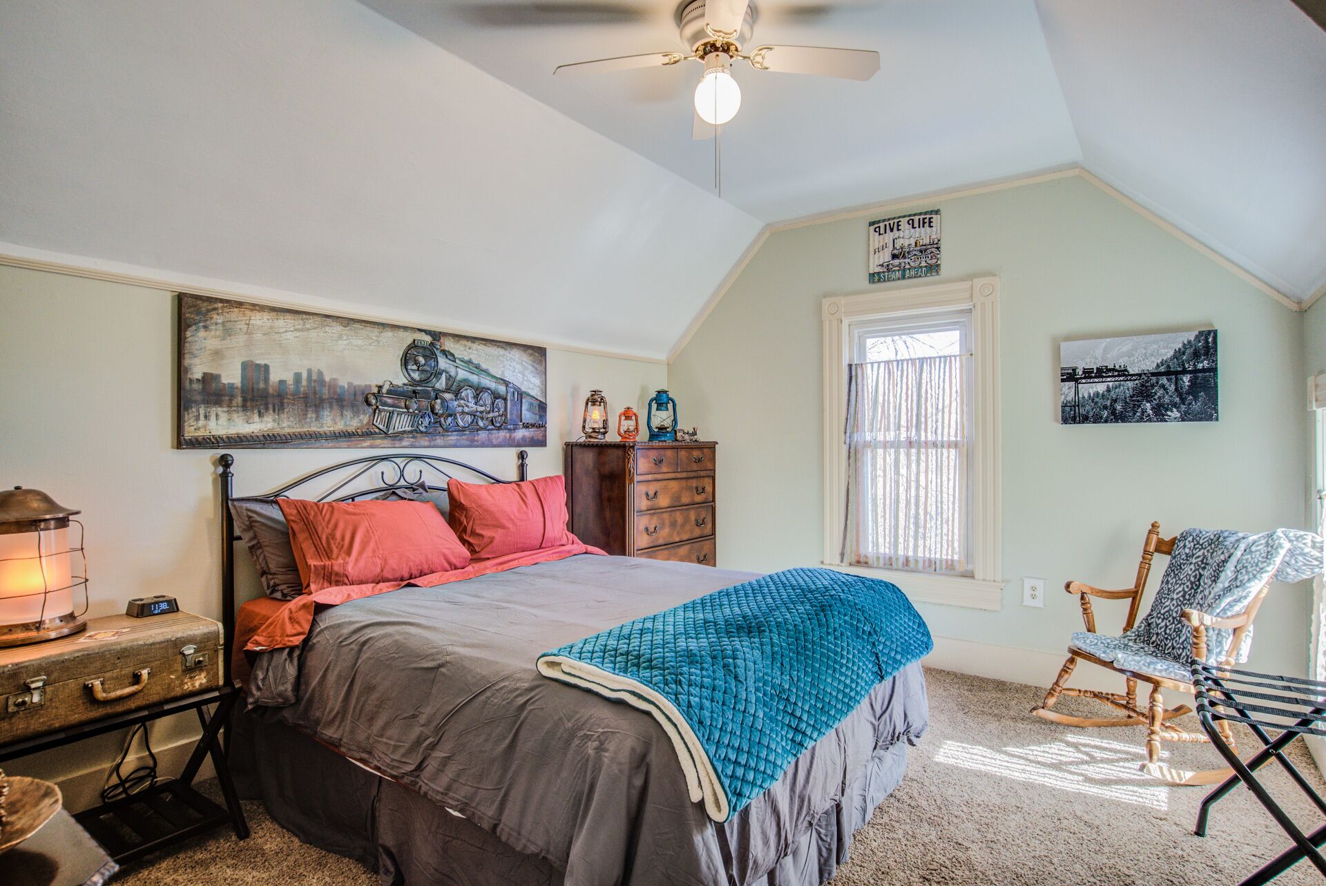 A bedroom with a bed, a dresser, a chair, and a ceiling fan.