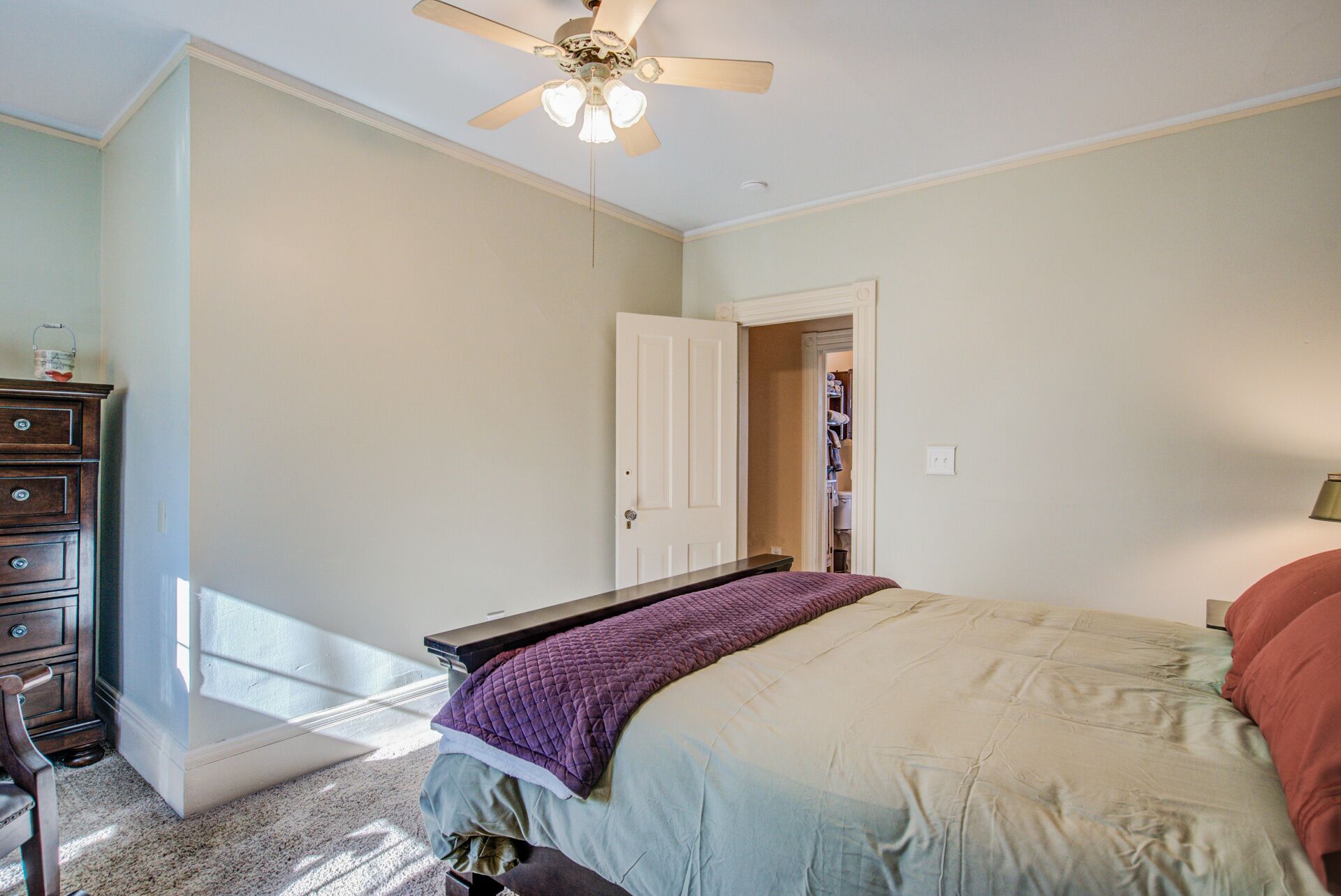 A bedroom with a bed, a dresser, a ceiling fan, and a door leading to a closet.