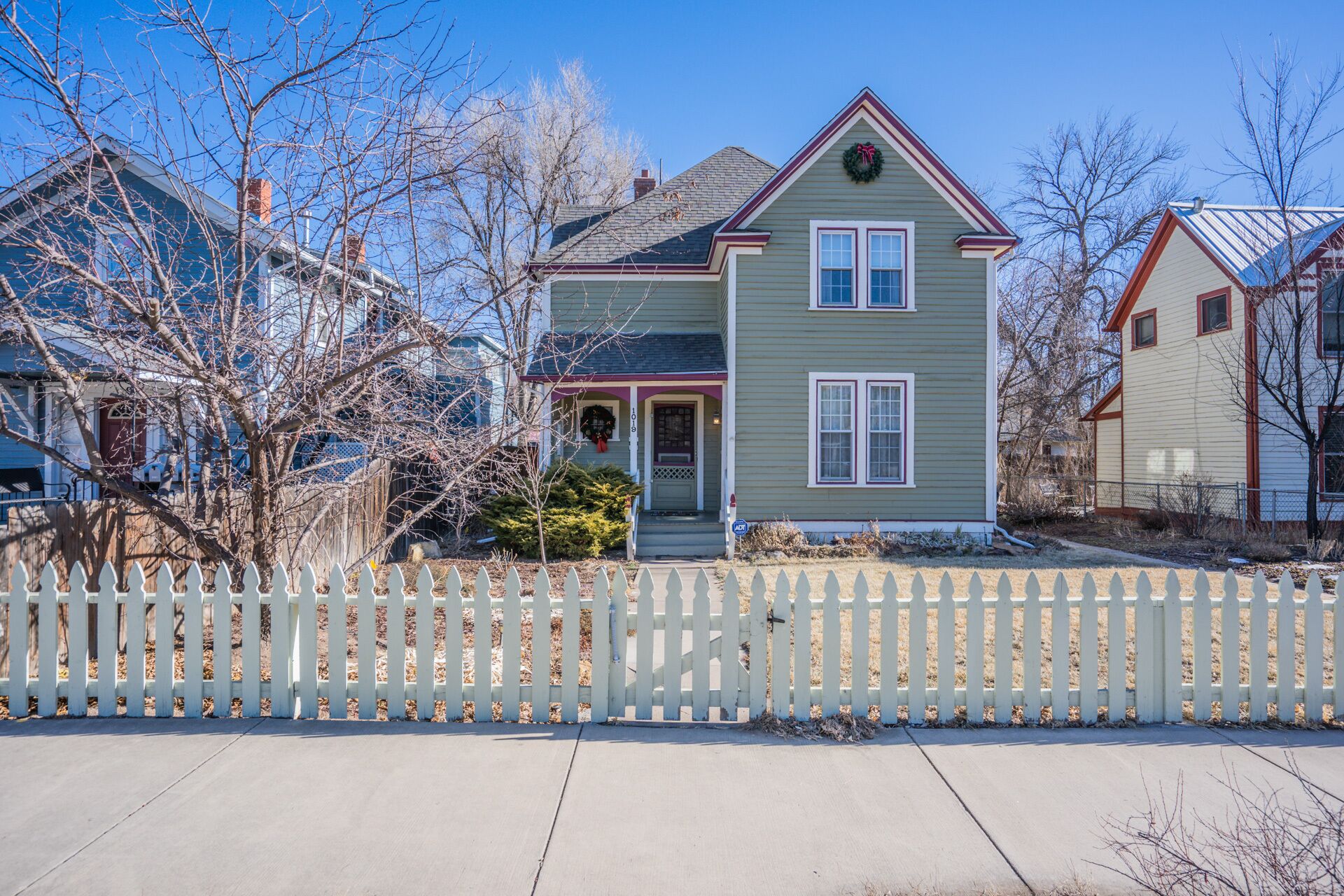 A two-story house with a front porch, a picket fence, and a clear blue sky.