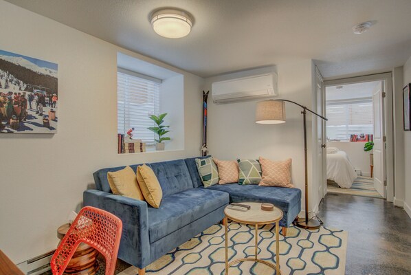 A living room with a blue sofa, a red chair, a patterned rug, and a painting on the wall.
