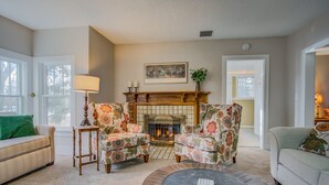 A cozy living room with a fireplace, floral armchairs, a round coffee table, and a sofa. - 5brmonument Historic Charmminutes To Hiking (Monument)