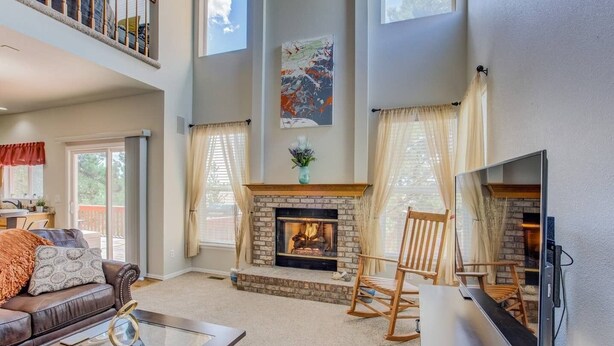 A spacious living room with a fireplace, a large TV, a high ceiling, and a balcony. - 4BR AF Academyw/hot Tub & Firepit (Colorado Springs)