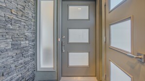 A hallway with a stone wall, a gray door with frosted glass panels, and a light fixture above the door. - Modern Rooftop Patio New-build Townhome in COS (Colorado Springs)
