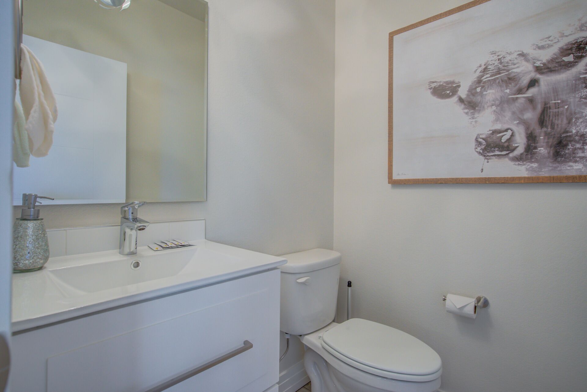 A bathroom with a white sink, mirror, and toilet. There is a framed artwork on the wall.