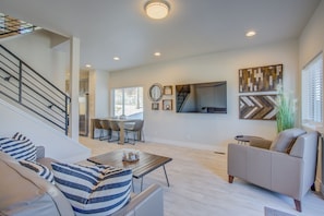 A spacious living room with a staircase, a dining area, and a sofa with striped cushions.