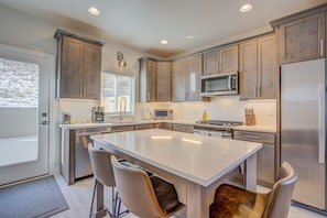 A modern kitchen with a central island, stainless steel appliances, and light wood cabinetry.
