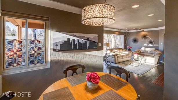A dining area with a round table, chairs, and a vase of flowers. There is a large window with stained glass and a cityscape painting on the wall. - 3bdmid-century Modernhot Tub, Grill, Close to DT (Colorado Springs)