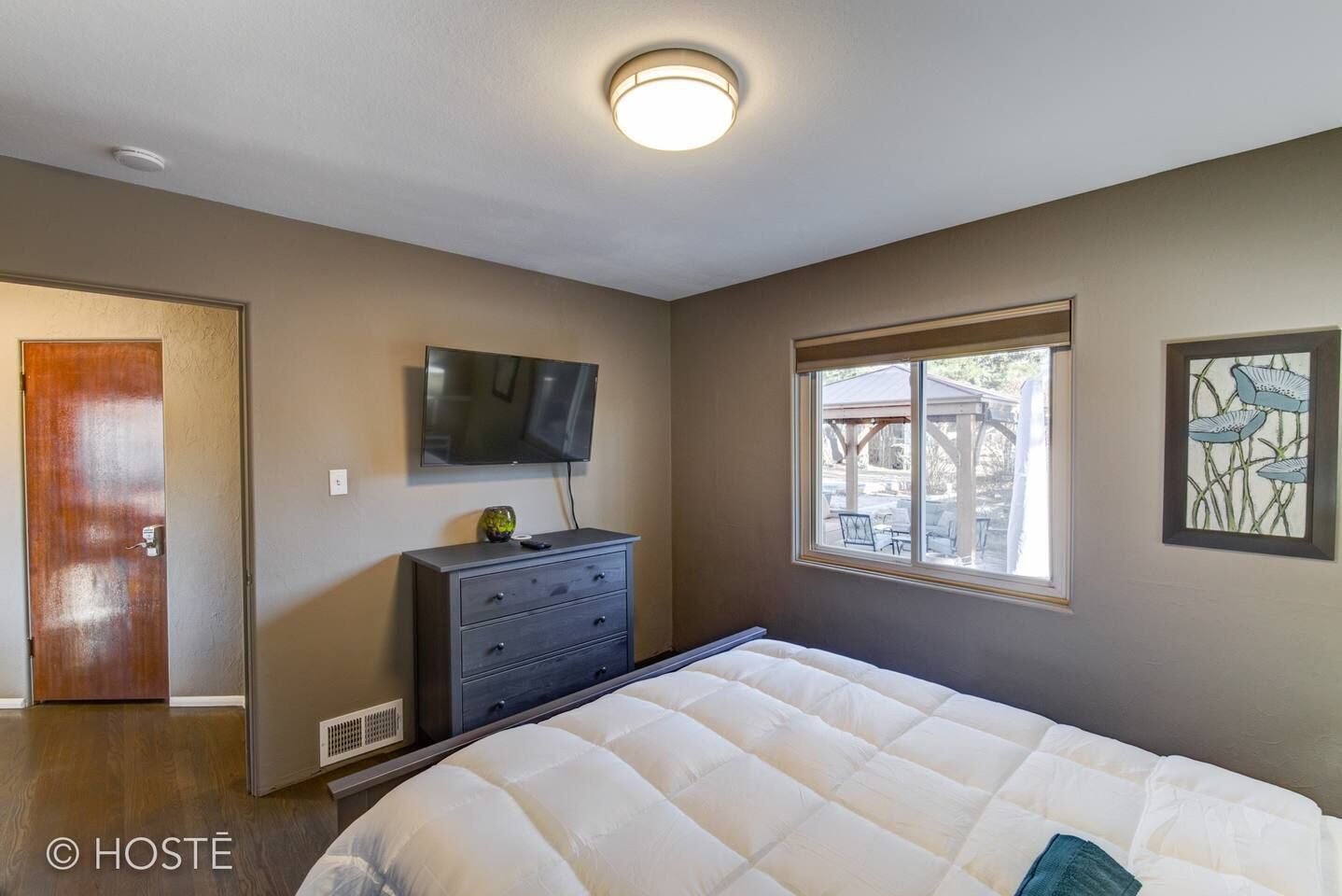 Une chambre à coucher comprenant un lit, une commode, un téléviseur et une fenêtre donnant sur une terrasse extérieure.