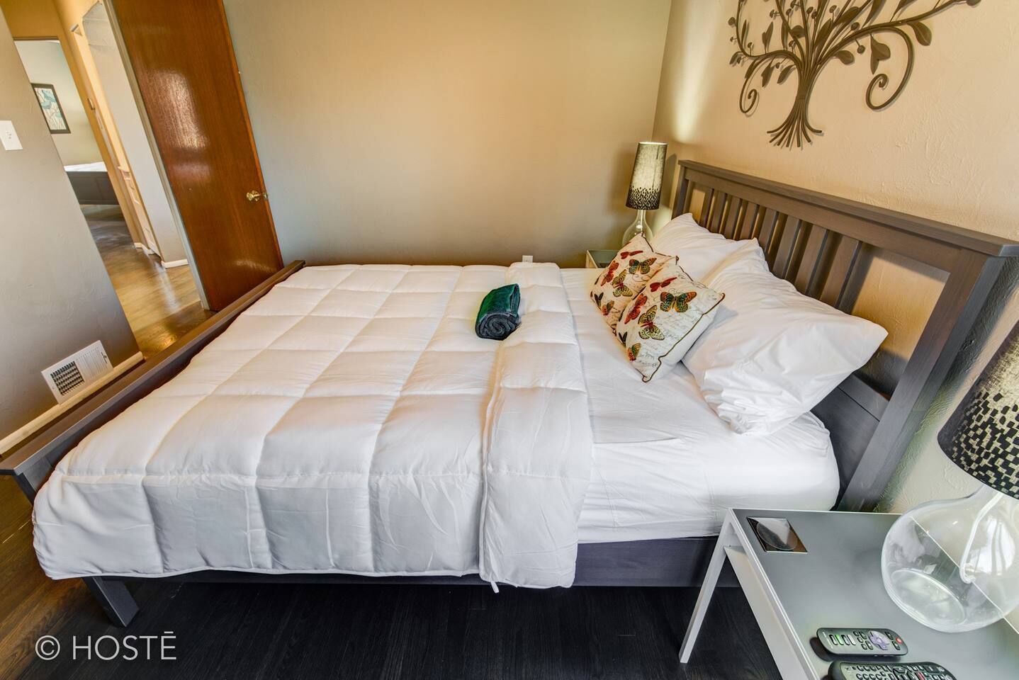 A neatly made bed with white linens, a green towel, and a decorative pillow with a floral pattern.