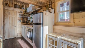 A compact kitchen with wooden cabinetry, a stainless steel refrigerator, and a small dining area with a woven bench.