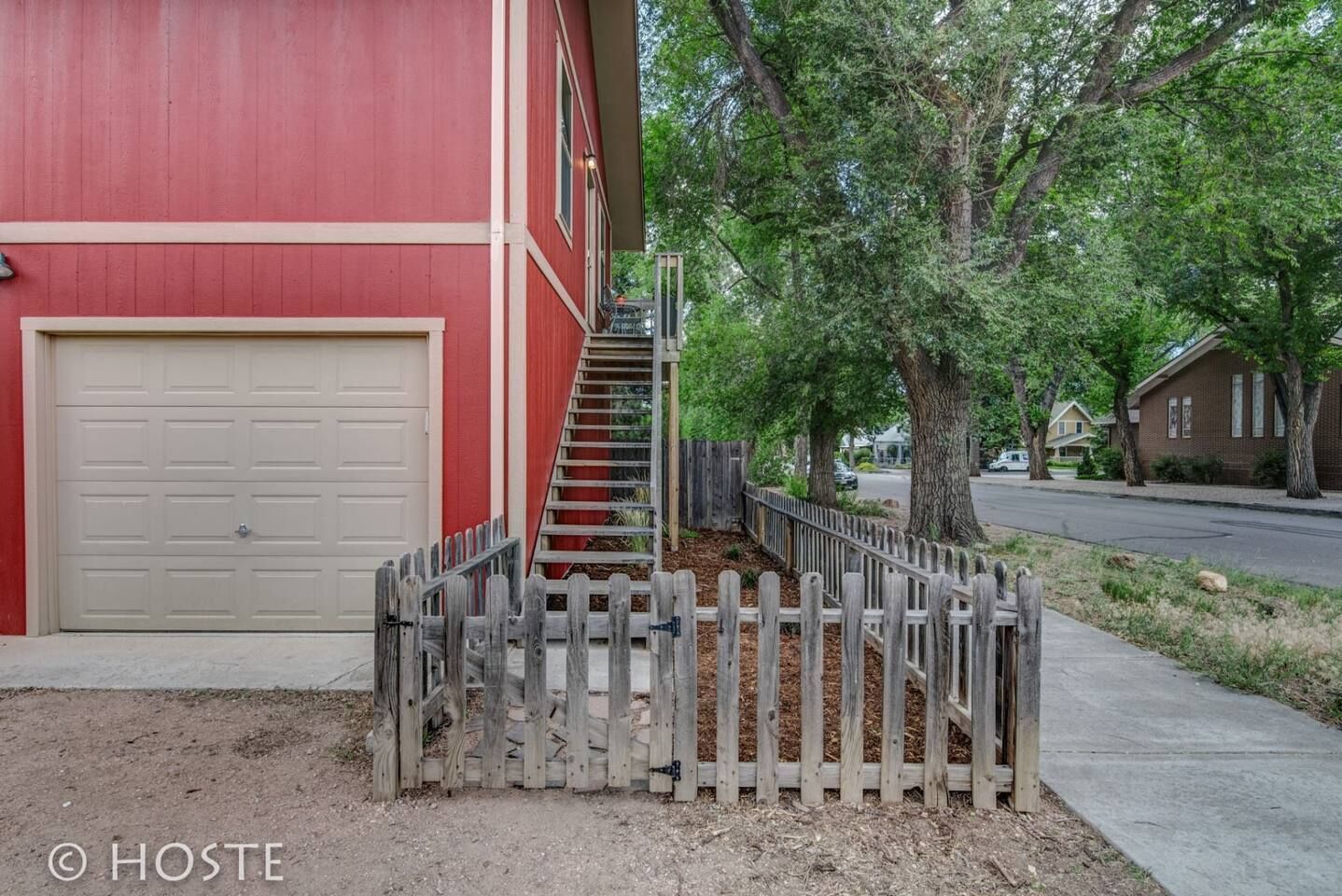 A red building with a white garage door, a wooden fence, and a staircase leading to the entrance.