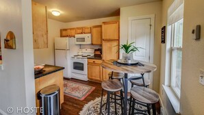 Une cuisine compacte avec des meubles en bois, un réfrigérateur blanc, un four à micro-ondes, une cuisinière et un coin repas comprenant une table ronde et des tabourets.