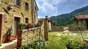 Un edificio de piedra con patio, plantas en macetas y vista a una ladera verde.