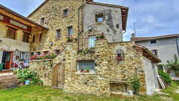 Un edificio in pietra con una scala di legno che conduce a una porta, immerso in un'area erbosa e decorato con piante in vaso.