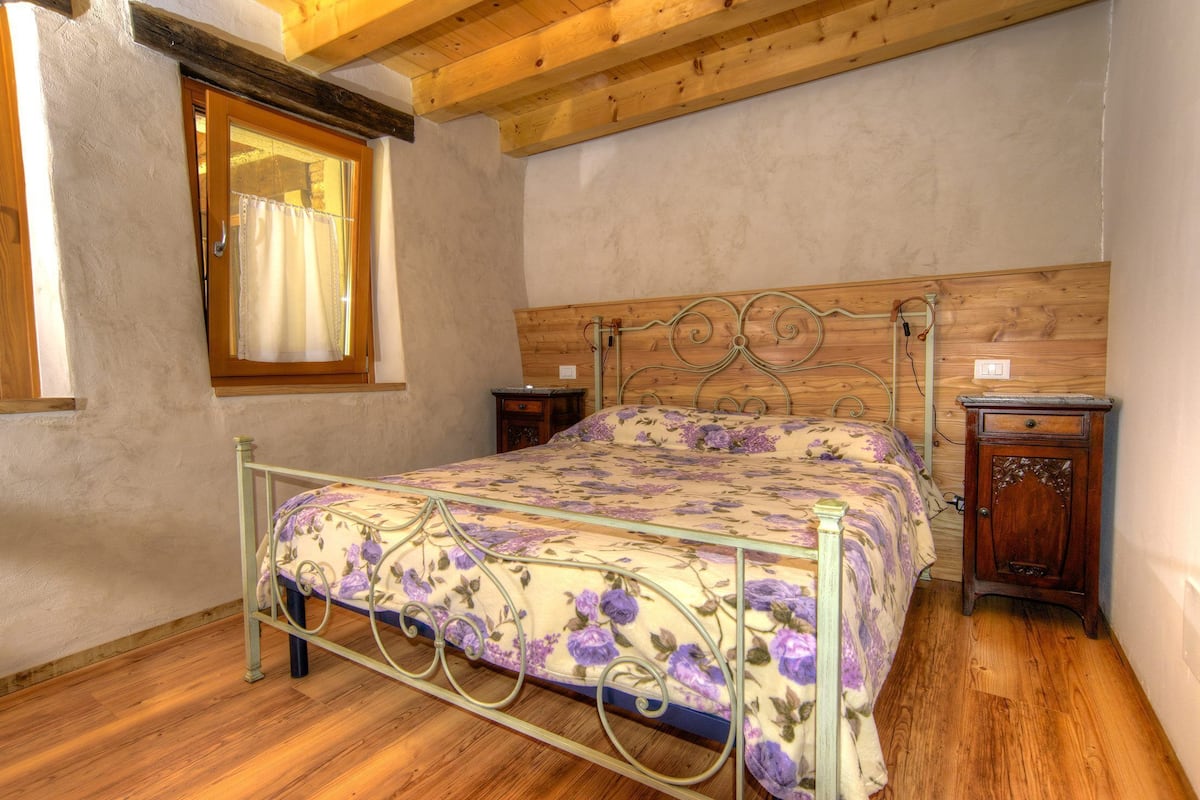 Un dormitorio con cama, cabecero de madera, una ventana con cortinas, una mesita de noche y un armario de madera.