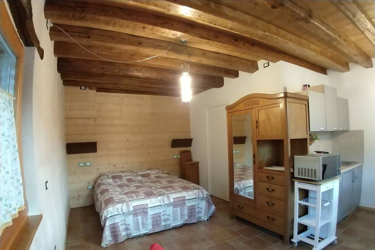 Un dormitorio con techo de madera, una cama con colcha estampada, un armario de madera, una mesita de noche blanca y un mueble blanco con microondas.