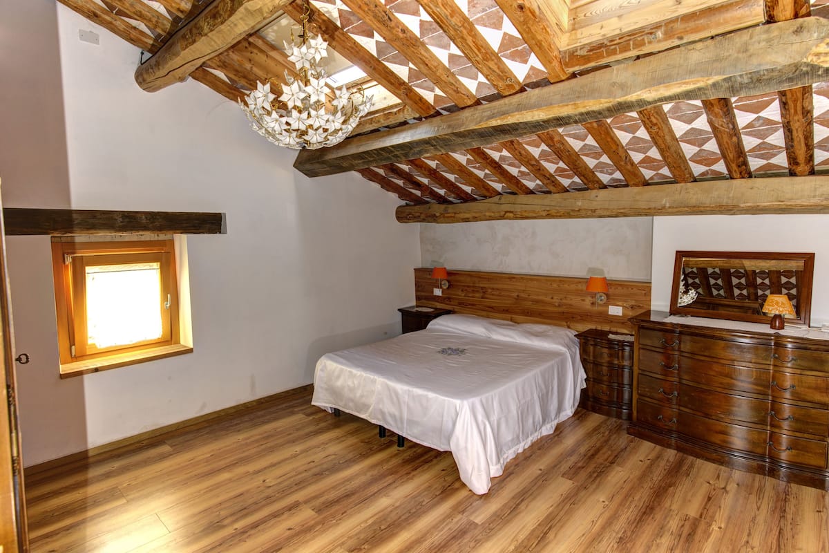 Un dormitorio con techo de madera, una cama, un aparador y un ventanal.