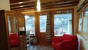 Una habitación acogedora con techo de madera, un sofá rojo, un armario de madera y un ventanal con vistas a árboles.