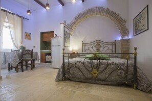 Una camera da letto con un arco in pietra, un letto con struttura in metallo, un tavolo da pranzo con sedie e un angolo cottura.