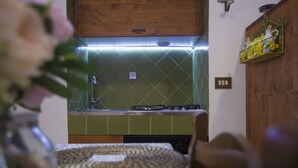 Una cocina con estufa a gas, salpicadero verde, armarios de madera y un estante pequeño con flores amarillas.