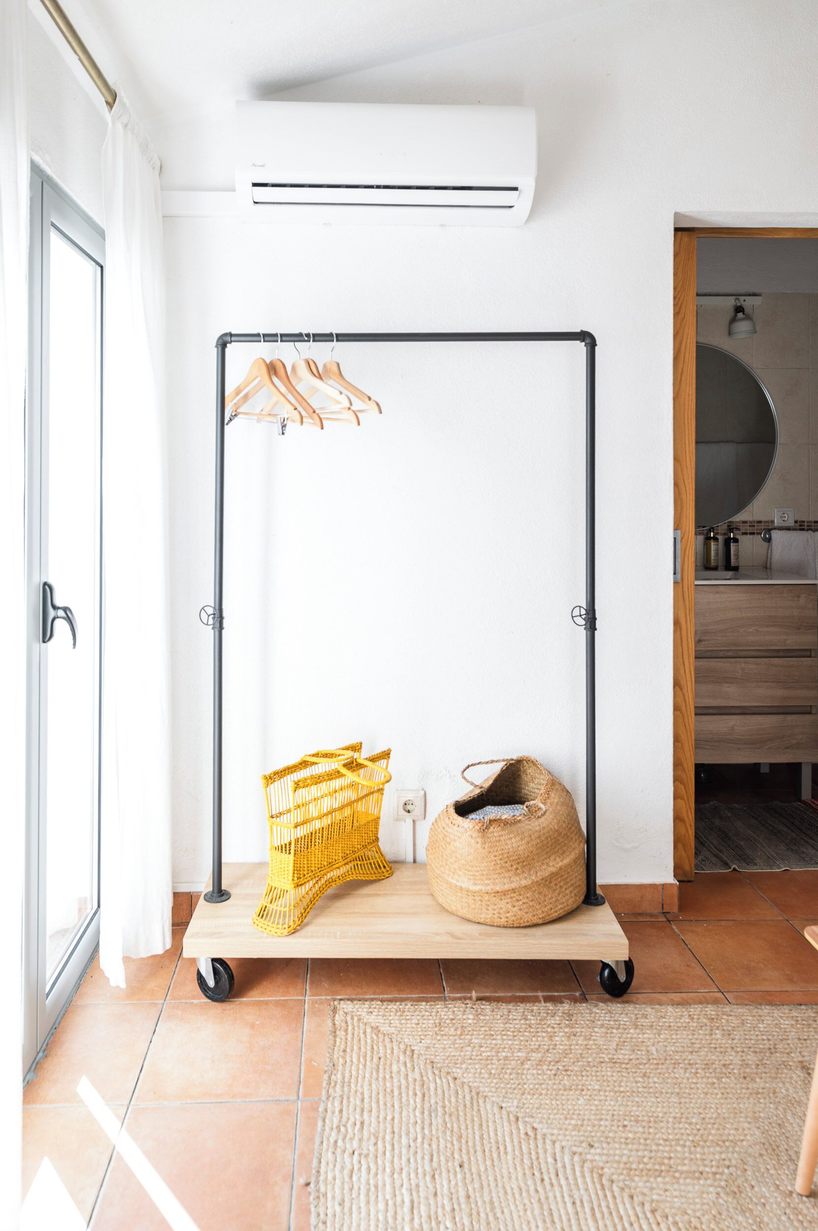 A room with a metal rack with clothes hangers, a yellow basket, and a woven bag on a wooden platform.