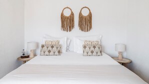 A neatly made bed with white bedding, two patterned pillows, and a pair of wall-mounted decorative items.
