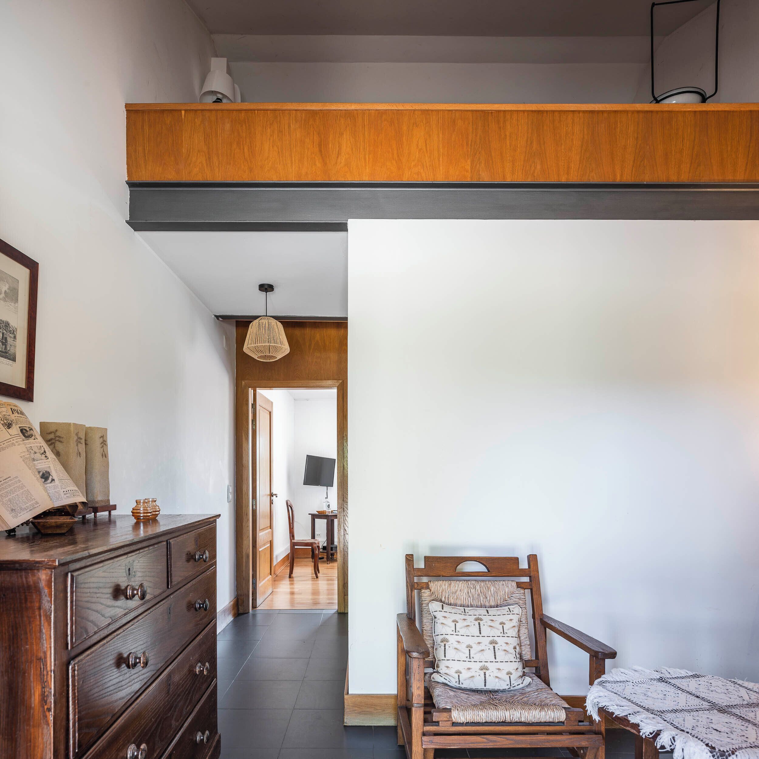 Un aparador de madera con cajones, una silla de mimbre con cojín y una mesita de noche con lámpara.