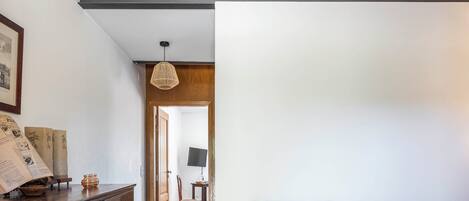 Un aparador de madera con cajones, una silla de mimbre con cojín y una mesita de noche con lámpara.