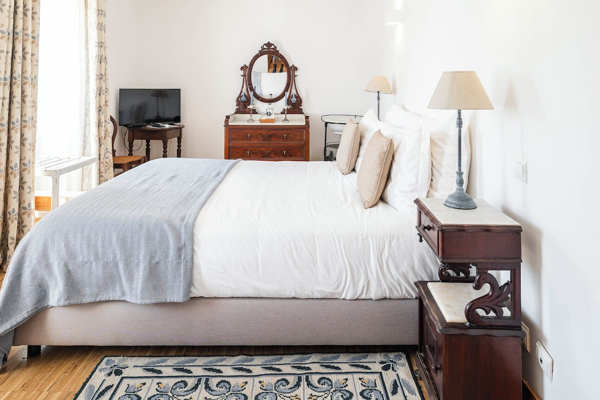 Une chambre bien rangée, avec un lit, une commode, un miroir, une lampe et un téléviseur.