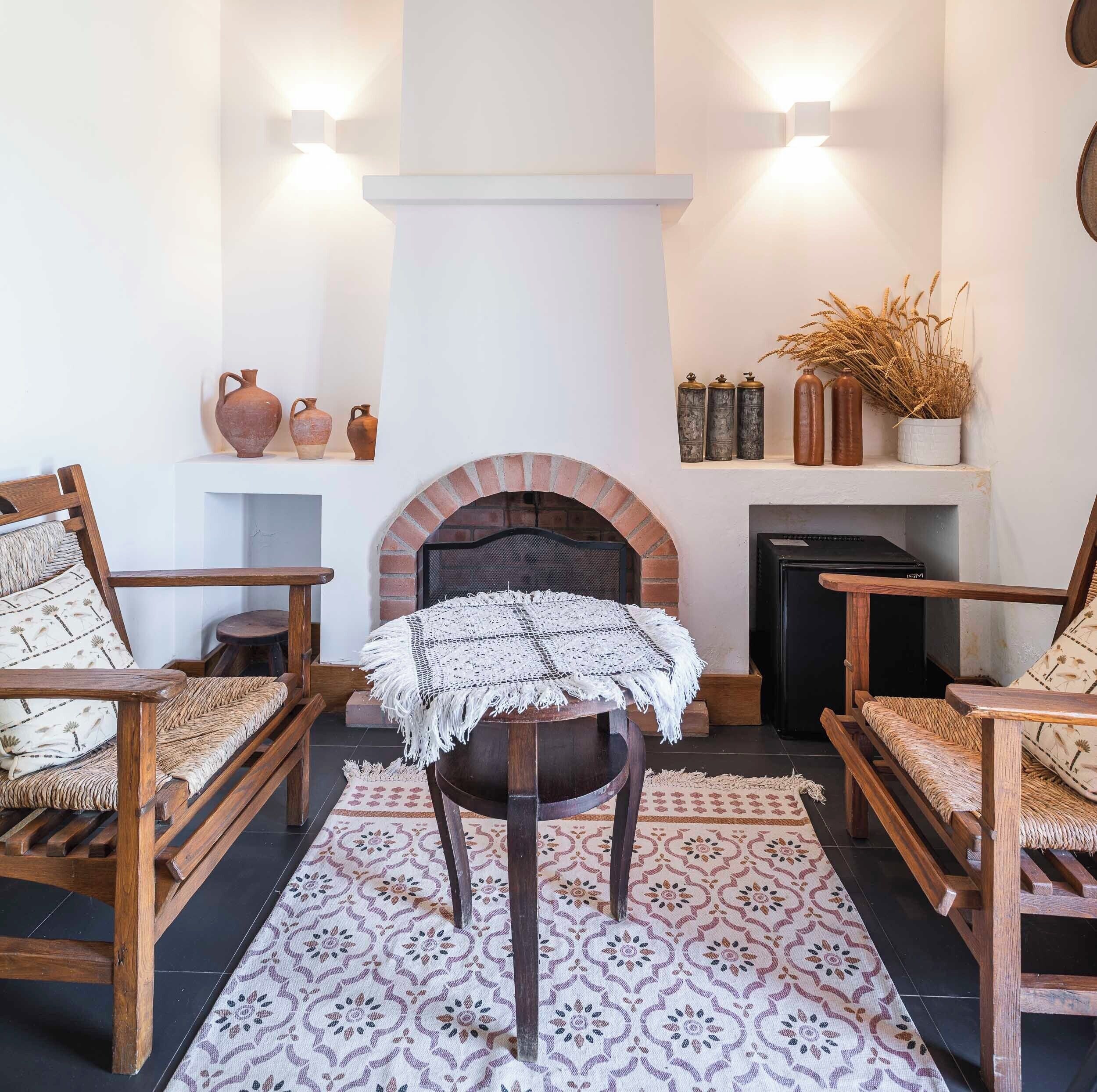 Un rincón acogedor con chimenea, sillas de madera y alfombra estampada.
