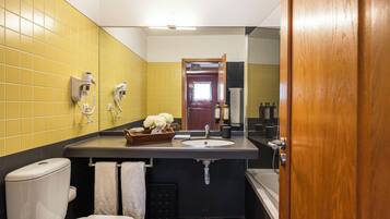 Un bagno con una parete rivestita di piastrelle gialle, un water bianco, un lavabo con uno specchio e una porta in legno.
