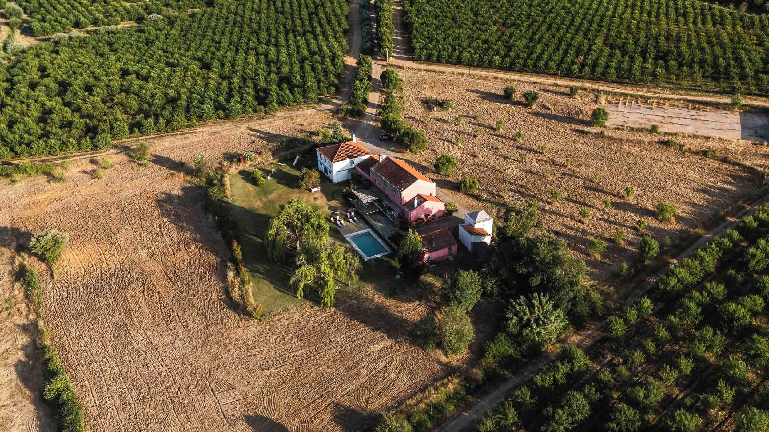 An aerial view of a property with a large house, a swimming pool, and surrounding agricultural fields.